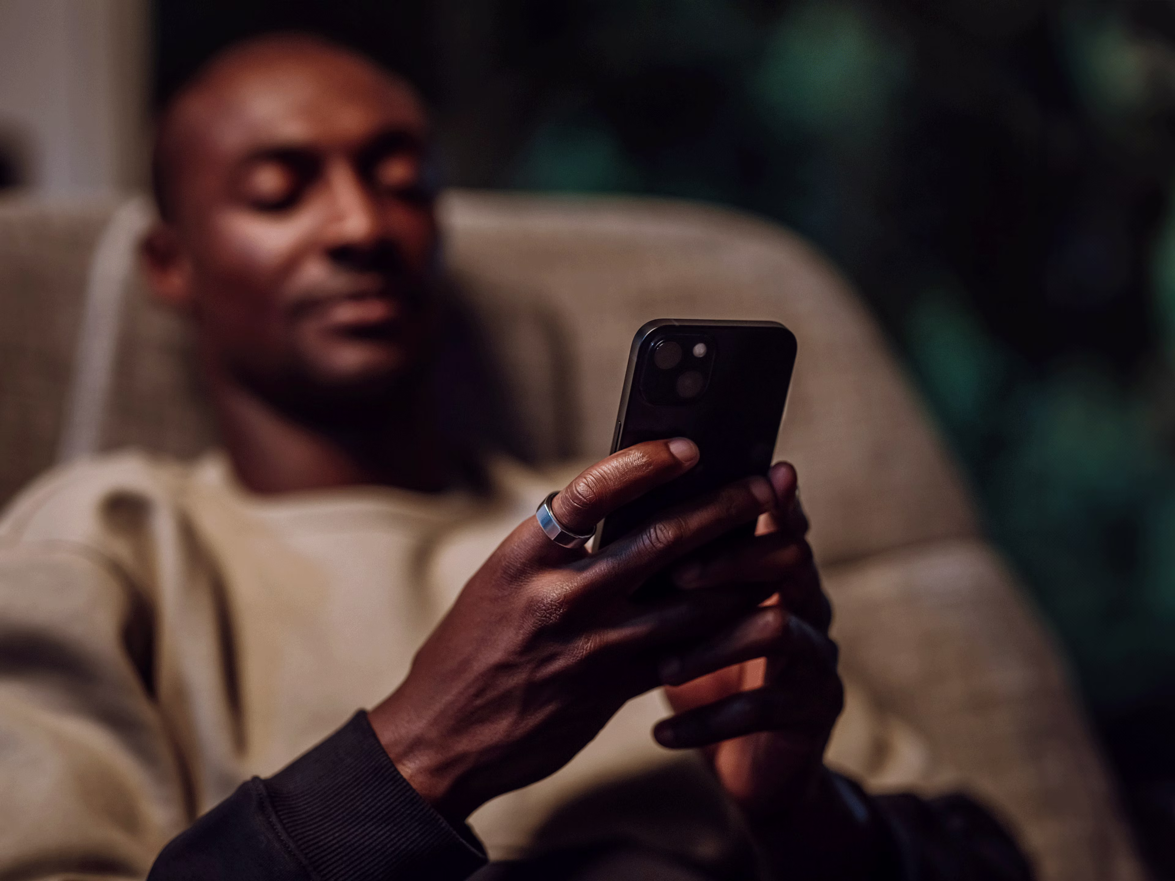 Homme assis dans un fauteuil inclinable, regardant l'écran de son smartphone, la KEORA Ring à l'index droit