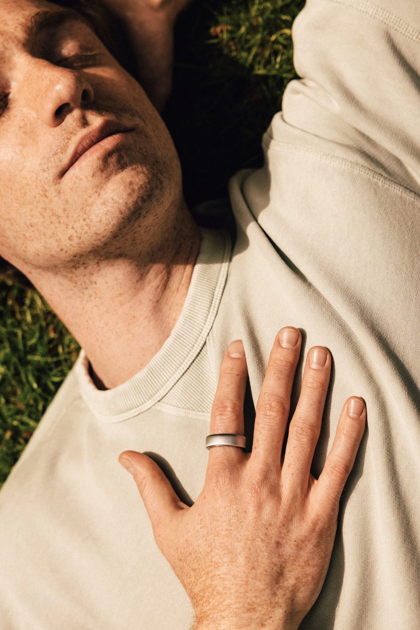Un homme est allongé sur l'herbe, la main droite sur la poitrine, et la KEORA Ring à l'index.