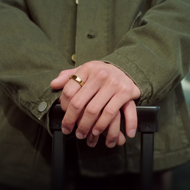 Gros plan sur les mains d’une personne reposant sur la poignée d’une valise, la KEORA Ring 6 Gold au doigt
