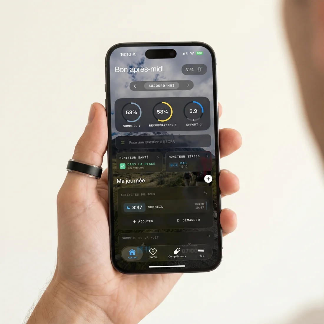 Hand wearing the KEORA ring holding an iPhone showing the KEORA app