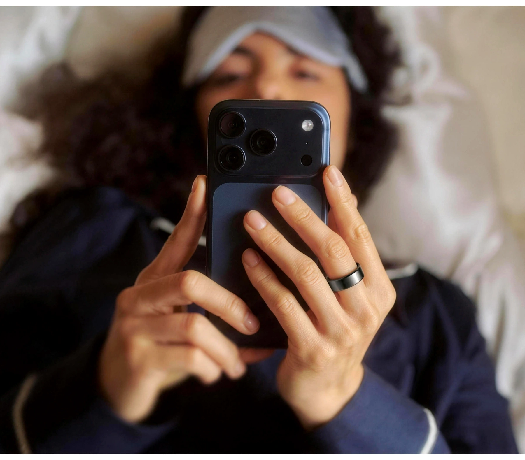 Une femme allongée qui regarde son téléphone, l’Oura Ring 5 au doigt.